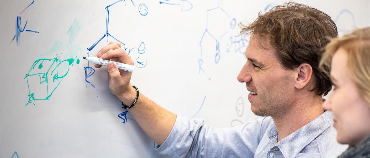 Prof. Dr. Job Boekhoven (l.) schreibt Strukturformeln an einem Whiteboard